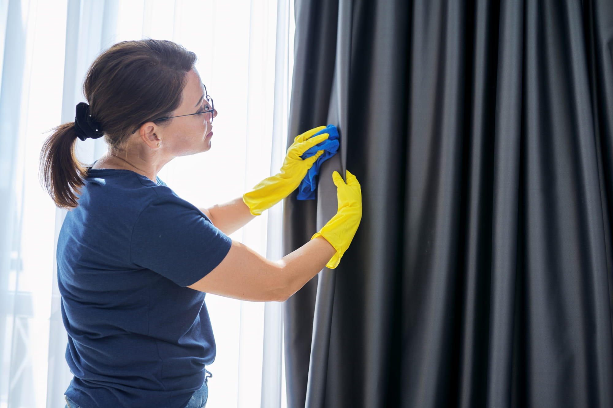 A woman cleaning black curtains thinking about how to remove mould from curtains effectively.